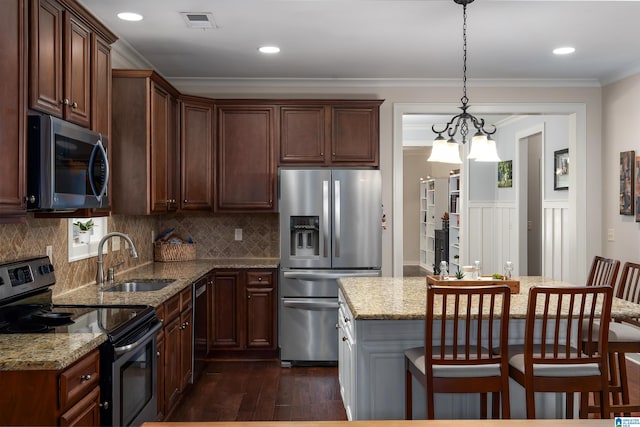 kitchen with light stone counters, hanging light fixtures, ornamental molding, appliances with stainless steel finishes, and a kitchen island