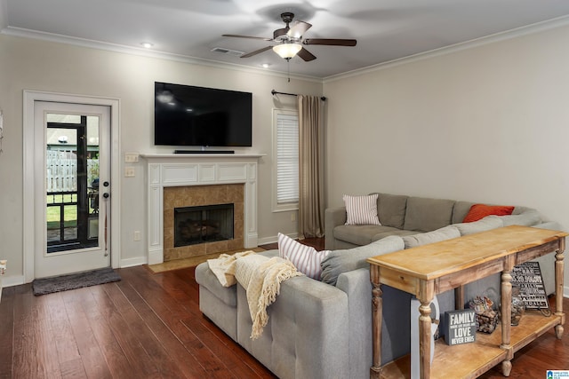 living room featuring dark hardwood / wood-style flooring, a tiled fireplace, ornamental molding, and ceiling fan