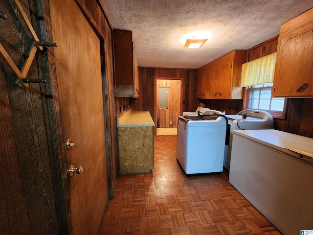 laundry room featuring dark parquet flooring, a textured ceiling, wood walls, separate washer and dryer, and cabinets