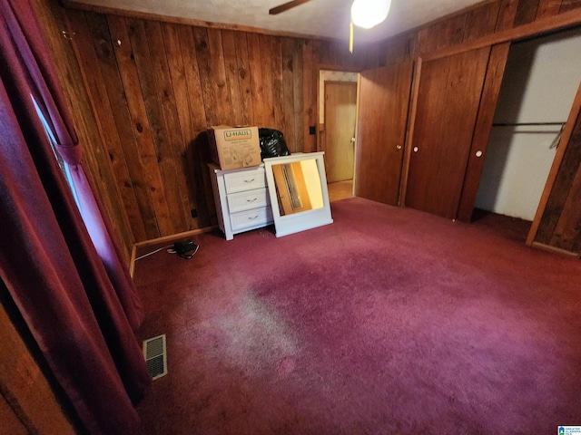 interior space featuring ceiling fan, dark colored carpet, and wooden walls