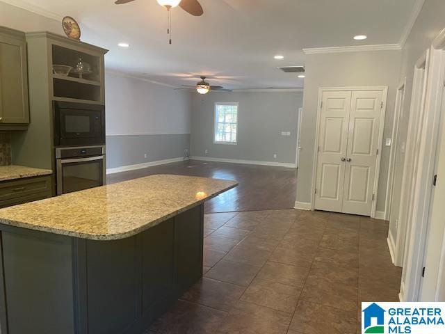 kitchen with stainless steel oven, black microwave, ornamental molding, ceiling fan, and light stone countertops