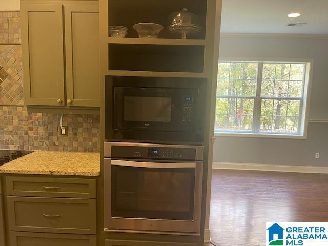 kitchen featuring tasteful backsplash, crown molding, black microwave, light stone countertops, and oven