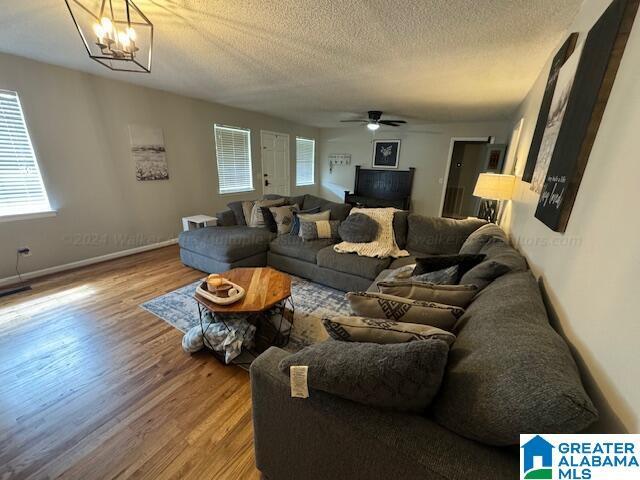 living room with hardwood / wood-style flooring, ceiling fan with notable chandelier, and a textured ceiling