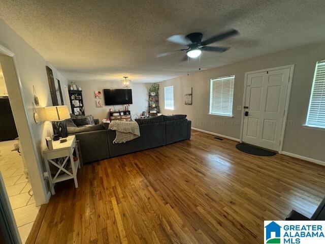 living room with ceiling fan, wood-type flooring, and a textured ceiling