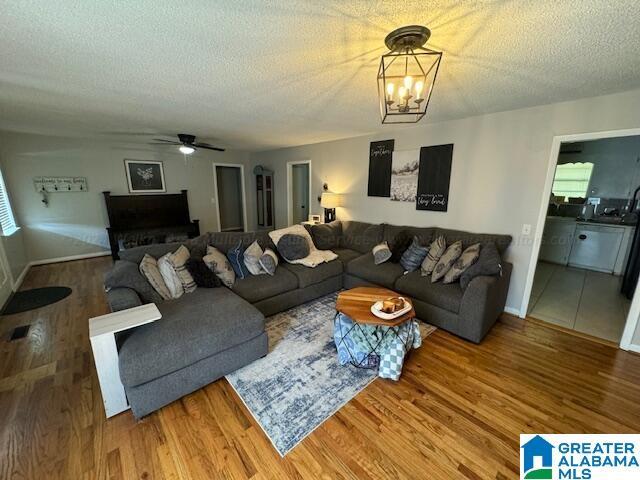 living room with hardwood / wood-style flooring, ceiling fan with notable chandelier, and a textured ceiling