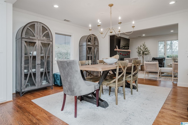 dining space featuring wood-type flooring, a notable chandelier, and crown molding