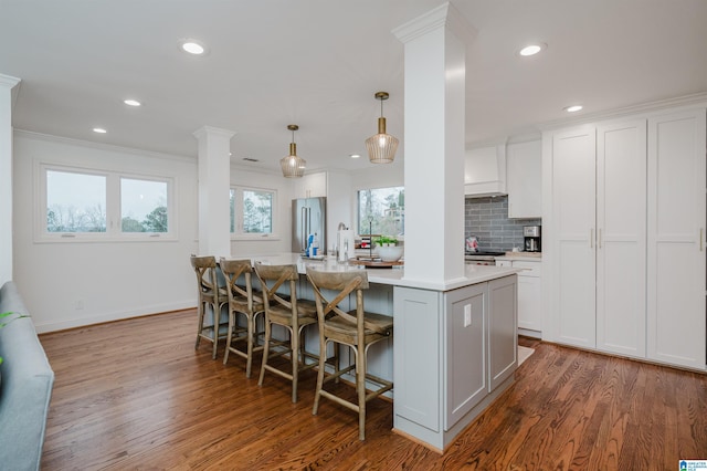 kitchen featuring high end refrigerator, an island with sink, pendant lighting, decorative columns, and white cabinets