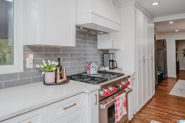 kitchen with white cabinets, high end stainless steel range oven, light hardwood / wood-style floors, crown molding, and custom range hood