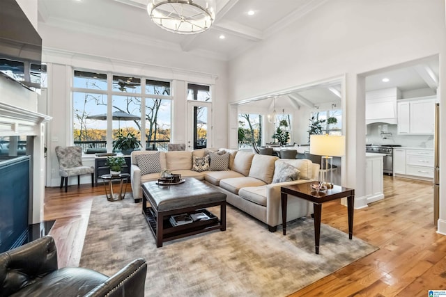 living room featuring beam ceiling, a towering ceiling, light hardwood / wood-style floors, and a chandelier