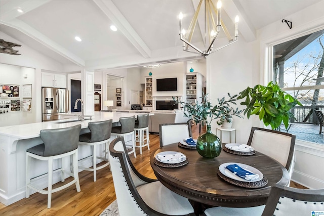 dining space featuring vaulted ceiling with beams, sink, an inviting chandelier, and light wood-type flooring