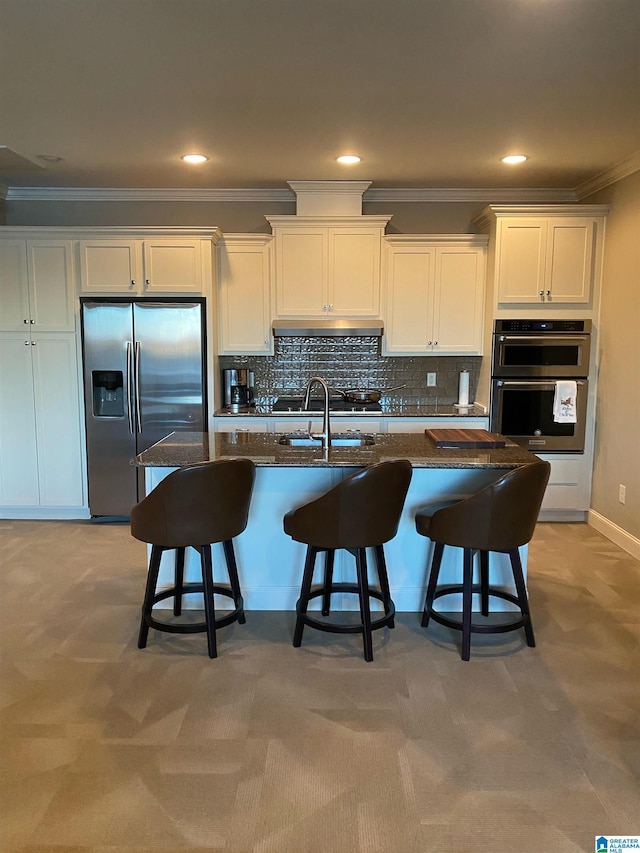 kitchen with stainless steel appliances, a center island with sink, white cabinets, and a kitchen bar