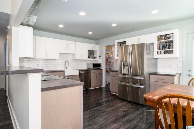 kitchen with sink, dark hardwood / wood-style floors, kitchen peninsula, stainless steel appliances, and white cabinets