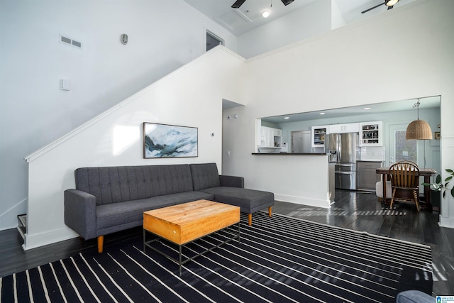 living room with dark hardwood / wood-style flooring, ceiling fan, and a high ceiling