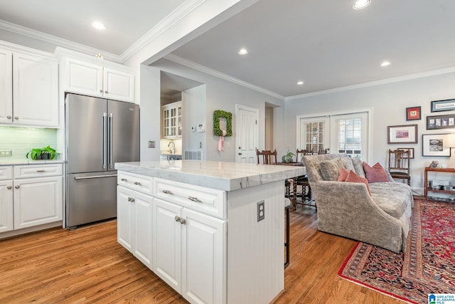 kitchen featuring high end fridge, white cabinetry, light wood-type flooring, a kitchen island, and backsplash