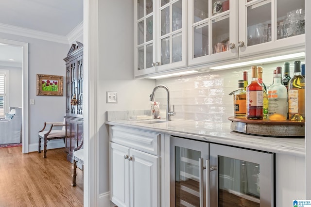 bar with sink, ornamental molding, beverage cooler, light stone countertops, and white cabinets