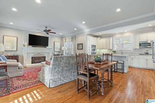 dining room featuring crown molding, ceiling fan, sink, and light wood-type flooring