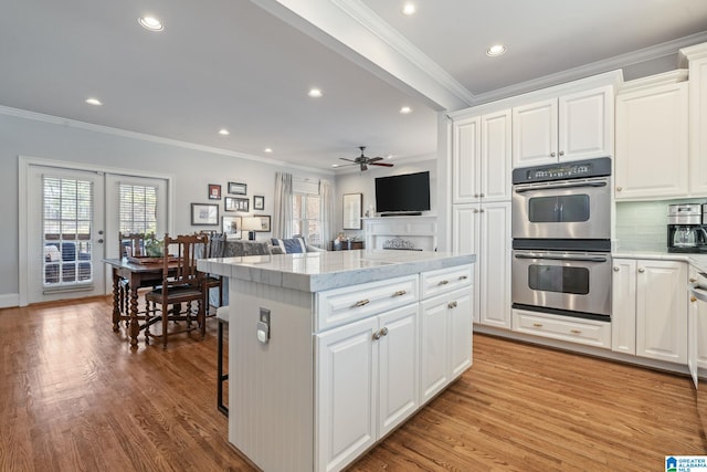 kitchen with double oven, crown molding, white cabinets, and a kitchen island