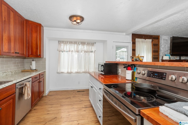 kitchen featuring appliances with stainless steel finishes, light wood-type flooring, white cabinets, decorative backsplash, and a textured ceiling