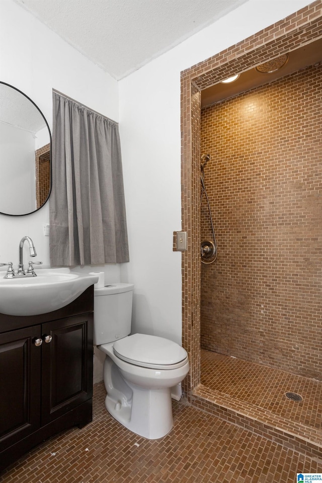 bathroom featuring vanity, a textured ceiling, toilet, and a tile shower