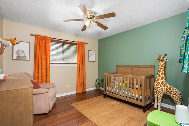 bedroom with ceiling fan, wood-type flooring, a nursery area, and a textured ceiling