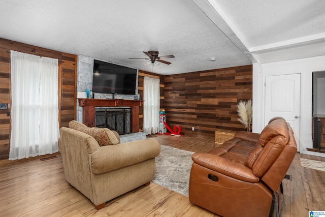 living room with a fireplace, wooden walls, a textured ceiling, and light wood-type flooring