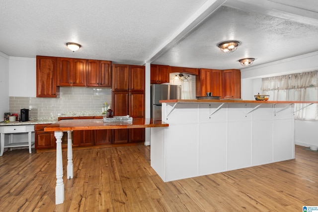 kitchen with a breakfast bar, stainless steel refrigerator, light wood-type flooring, decorative backsplash, and a textured ceiling