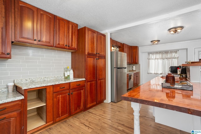 kitchen with light stone counters, light hardwood / wood-style flooring, a textured ceiling, and appliances with stainless steel finishes