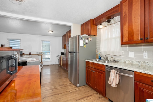 kitchen with appliances with stainless steel finishes, tasteful backsplash, sink, light hardwood / wood-style floors, and a textured ceiling