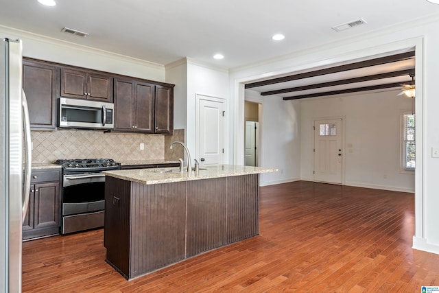 kitchen featuring sink, light stone counters, an island with sink, stainless steel appliances, and beam ceiling