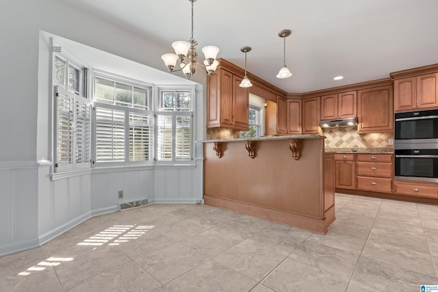 kitchen featuring a breakfast bar, hanging light fixtures, backsplash, kitchen peninsula, and stainless steel double oven