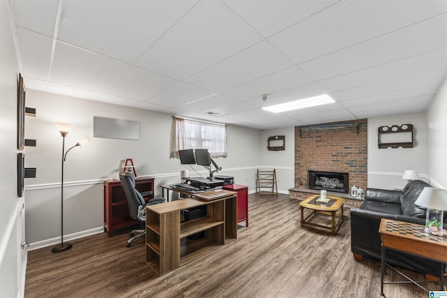 home office with a drop ceiling, hardwood / wood-style floors, and a brick fireplace