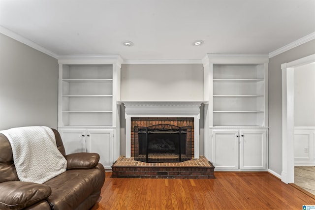 living room with crown molding, wood-type flooring, and a brick fireplace