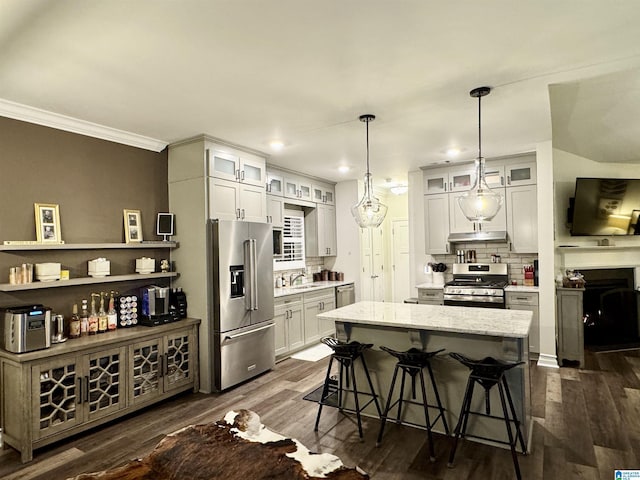 kitchen with a kitchen island, pendant lighting, decorative backsplash, stainless steel appliances, and light stone countertops