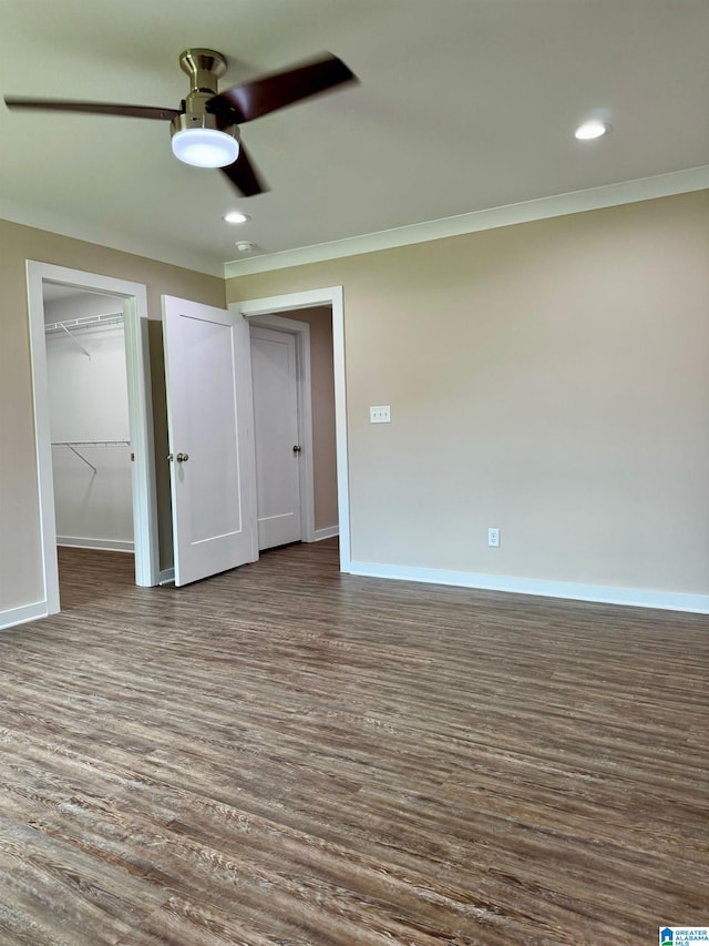 unfurnished bedroom featuring ornamental molding, dark wood-type flooring, ceiling fan, and a spacious closet