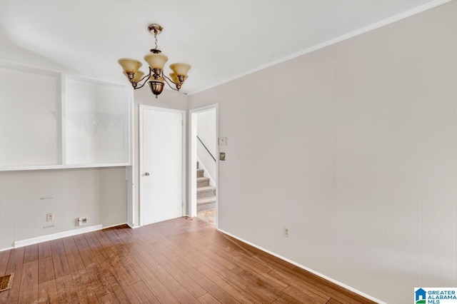 empty room with hardwood / wood-style flooring, crown molding, and a chandelier