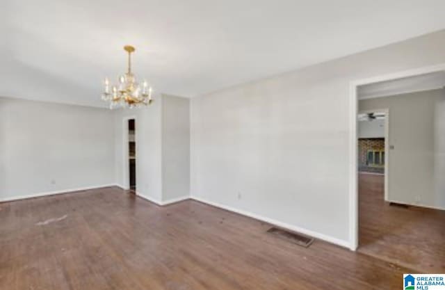 empty room with dark hardwood / wood-style floors and an inviting chandelier