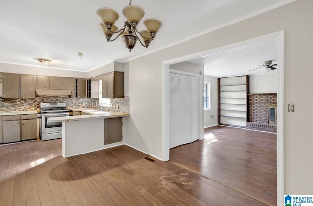 kitchen with sink, dark hardwood / wood-style flooring, a brick fireplace, stainless steel range with electric cooktop, and kitchen peninsula