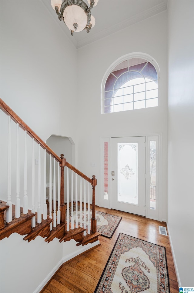 entryway with an inviting chandelier, crown molding, wood-type flooring, and a high ceiling