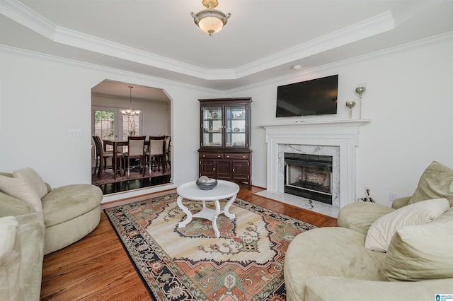 living room featuring hardwood / wood-style flooring, a premium fireplace, ornamental molding, a raised ceiling, and a chandelier