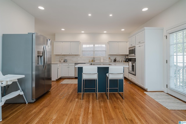 kitchen featuring light wood-type flooring, stainless steel appliances, white cabinets, and a kitchen island