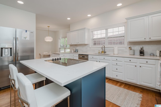 kitchen with sink, appliances with stainless steel finishes, white cabinetry, hanging light fixtures, and decorative backsplash