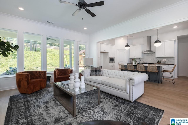 living room featuring hardwood / wood-style floors, crown molding, sink, and ceiling fan