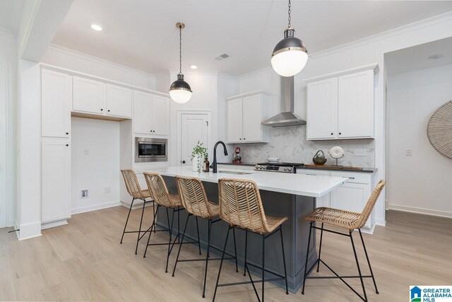 kitchen featuring an island with sink, white cabinetry, sink, stainless steel appliances, and wall chimney exhaust hood
