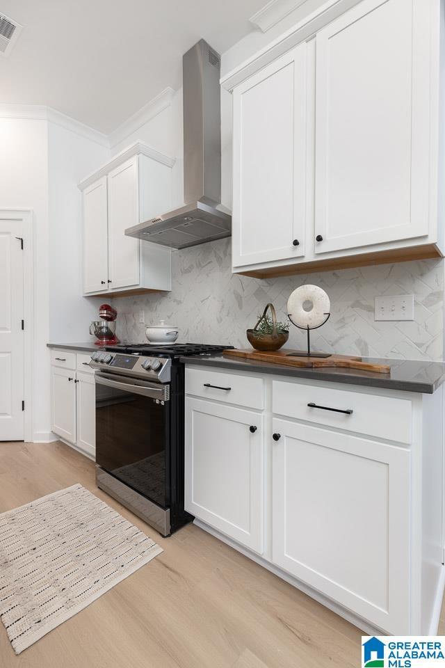 kitchen featuring white cabinets, stainless steel range, tasteful backsplash, and wall chimney range hood