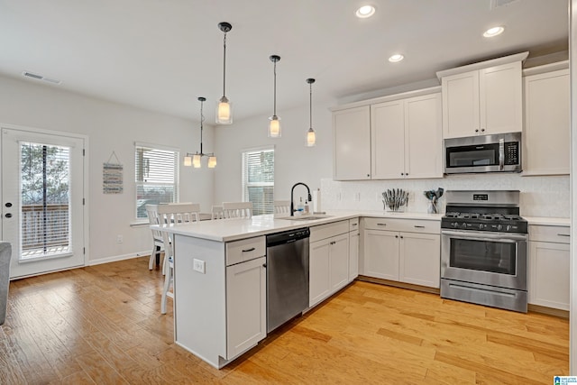 kitchen featuring decorative light fixtures, stainless steel appliances, kitchen peninsula, and white cabinets