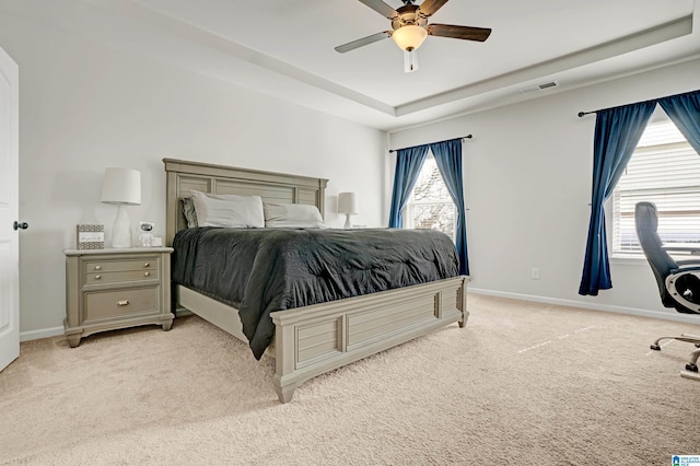 bedroom with a raised ceiling, light colored carpet, and ceiling fan