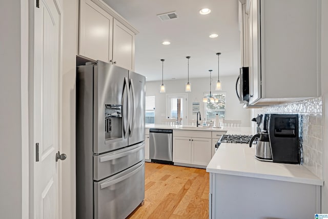 kitchen with sink, light hardwood / wood-style flooring, hanging light fixtures, stainless steel appliances, and kitchen peninsula