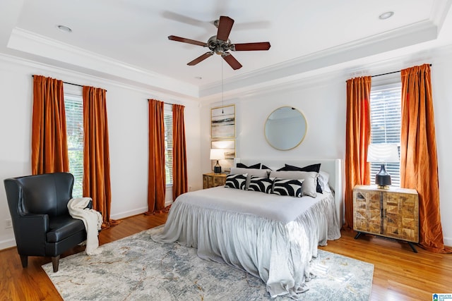 bedroom featuring crown molding, light hardwood / wood-style floors, a raised ceiling, and ceiling fan