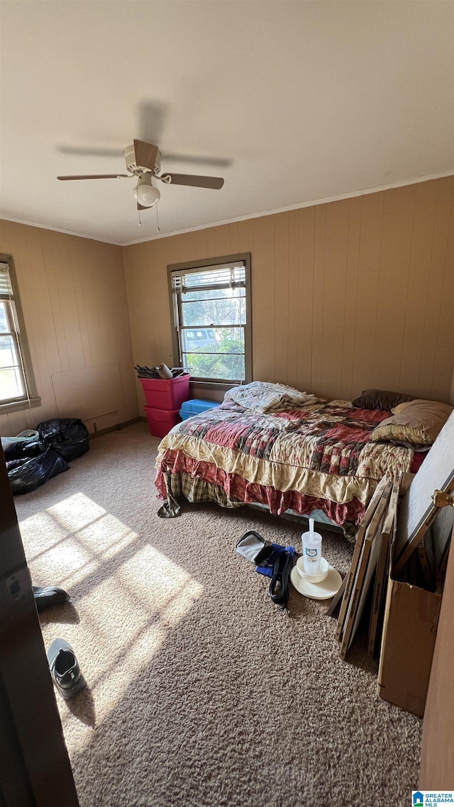 bedroom featuring ceiling fan, wooden walls, carpet, and multiple windows