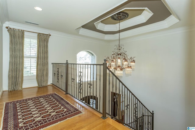 hall featuring an inviting chandelier, hardwood / wood-style floors, crown molding, and a raised ceiling